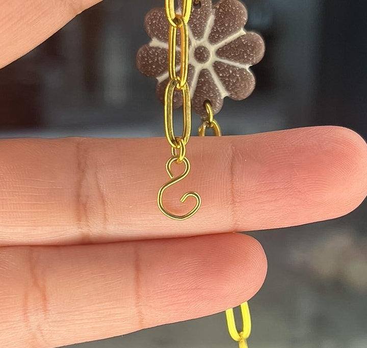 Hand holding a small gold chain with a flower-shaped pendant.